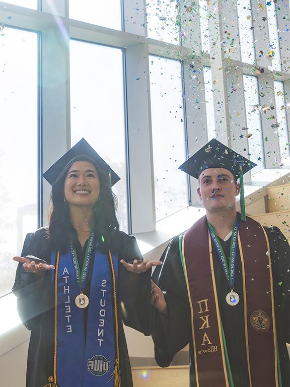 两名威斯康星大学毕业生戴着学士帽，身穿学士服，正在扔五彩纸屑