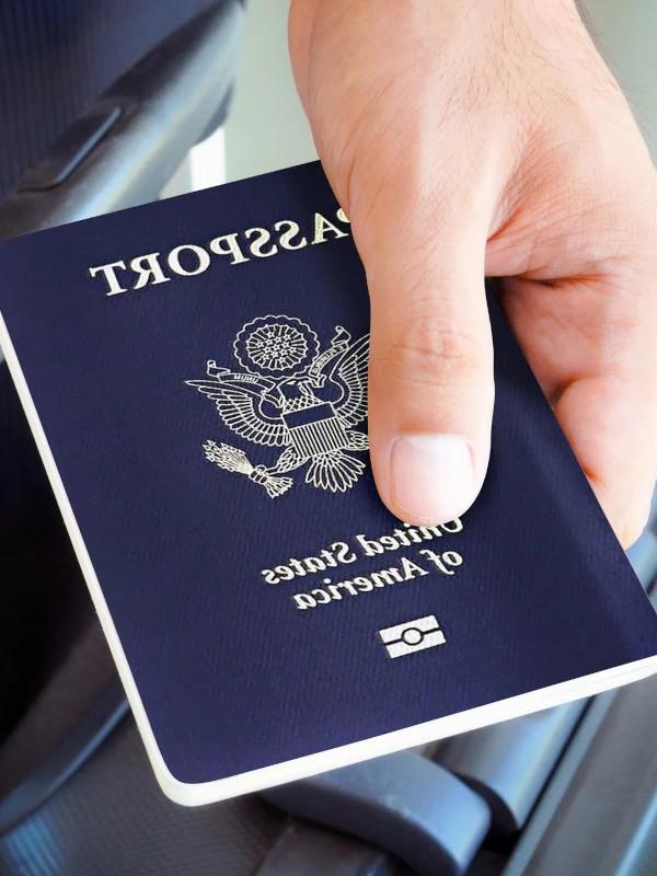 A hand holds a US Passport on top of a suitcase.